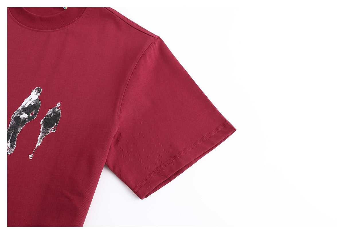 Close-up of a burgundy T-shirt's crew neck, short sleeve and partial black-and-white figure print.