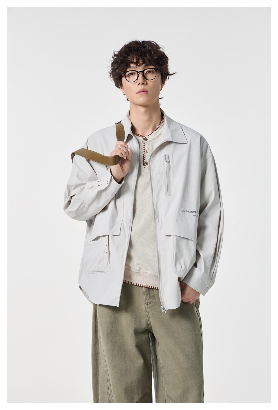 Closer view of a model wearing a pale gray collared jacket with front zipper, chest zip pockets and large flap pockets.