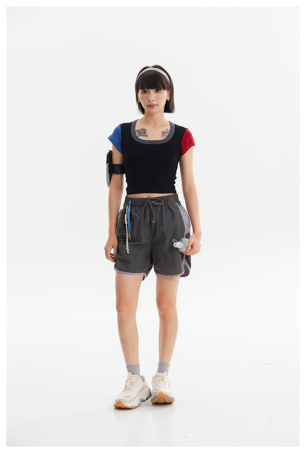 Full-length front view of a model in dark gray running shorts with lavender side panels and a black top with blue and red