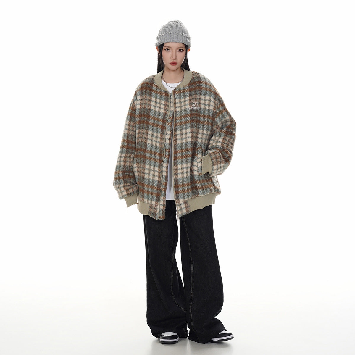 Model wearing a beige-trimmed plaid zip jacket in cream, gray, and rust, with black wide-leg pants.