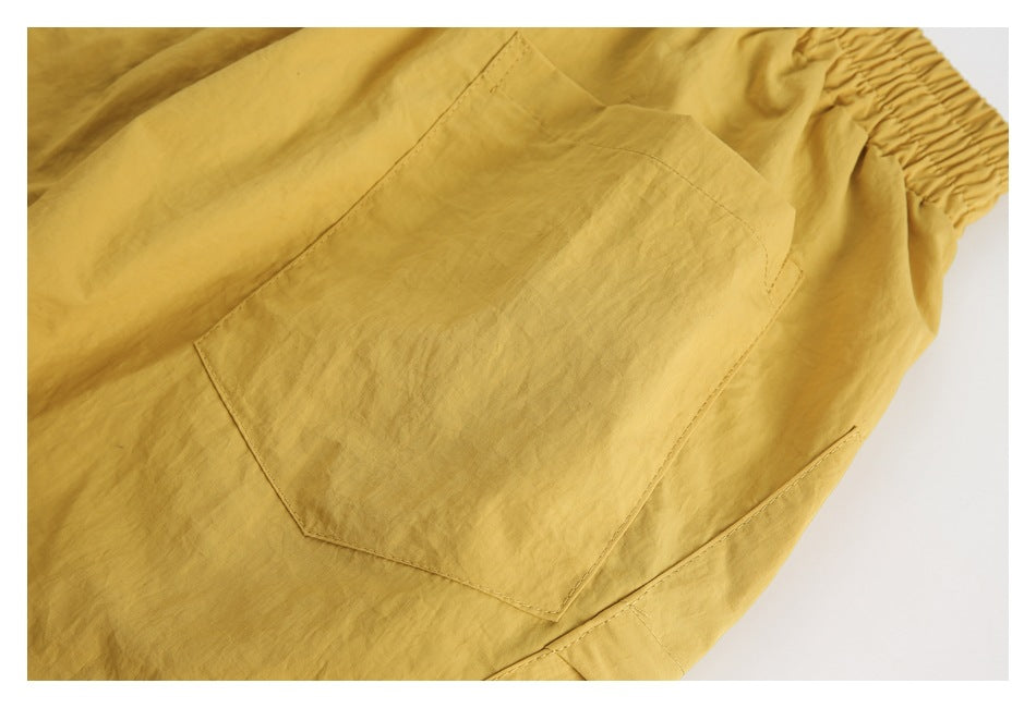 Close-up of mustard-yellow garment with a large stitched pocket and gathered elastic edge.