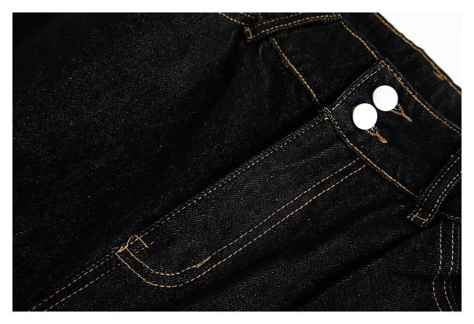 Close-up of black jeans showing a curved front pocket, gold stitching and two silver waist buttons.