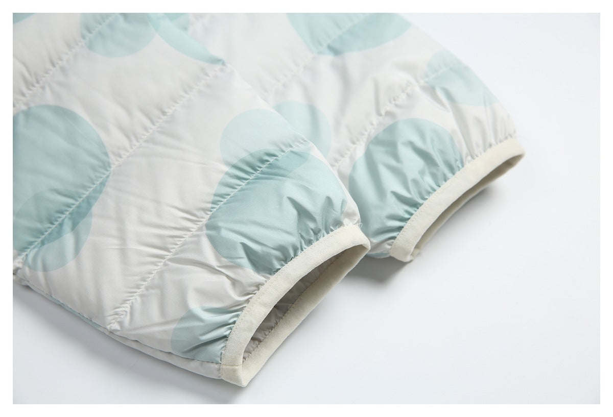 Close view of a pale aqua circle-print puffer jacket sleeve ending in a cream-trimmed cuff.