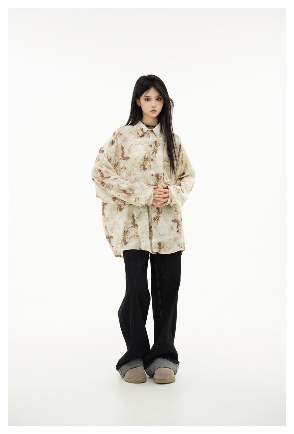 Full-length model wearing an oversized cream and brown abstract-print button-up shirt, black wide-leg jeans, and taupe shoes.