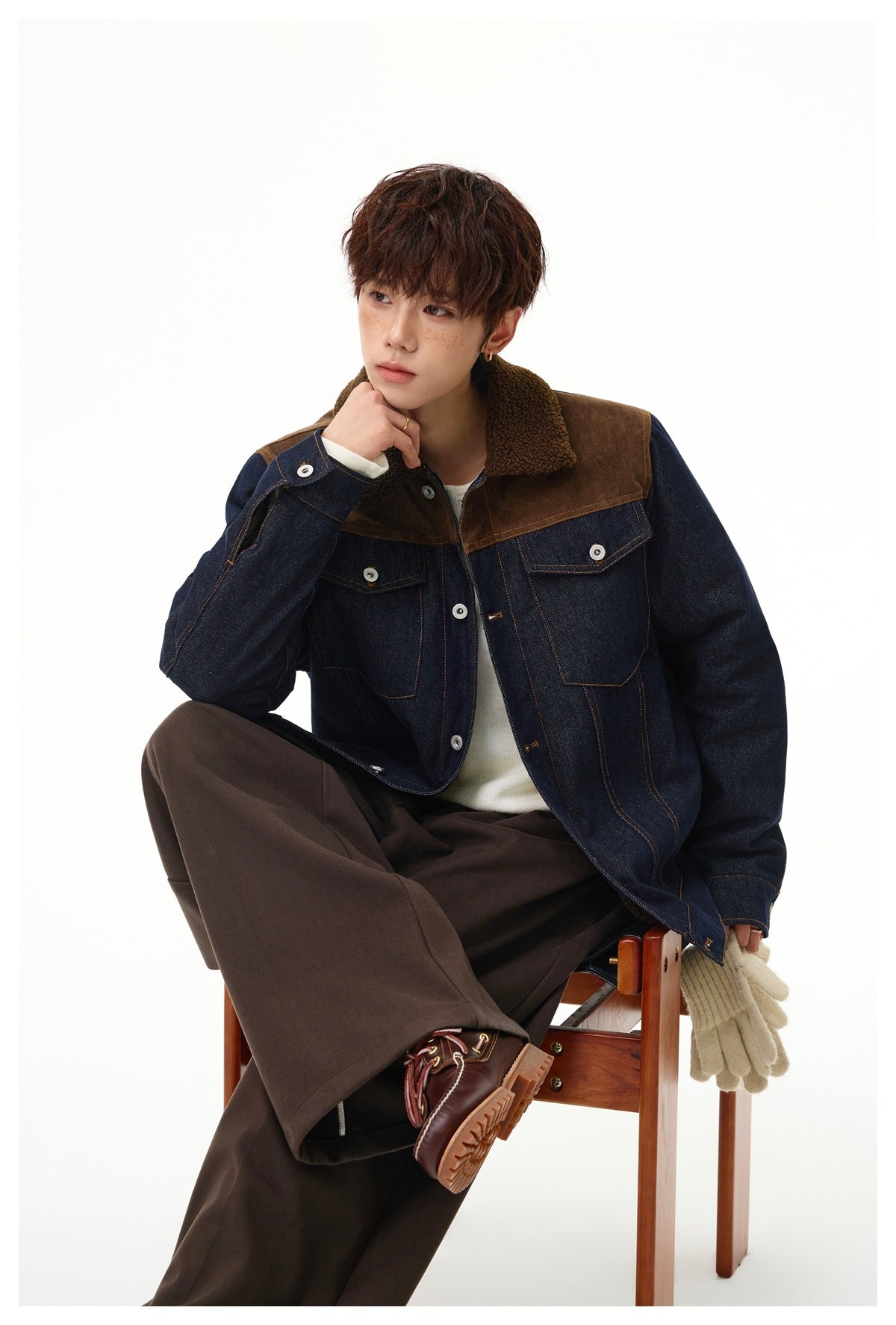 Model seated on a wooden stool wearing a denim jacket with brown yoke and fleece-like collar over a white top