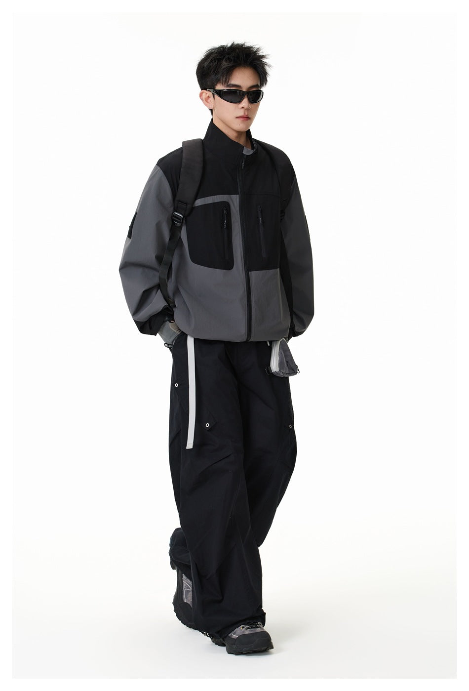 Three-quarter view of a model wearing a black and charcoal-gray zip jacket with a high collar and zip pockets.