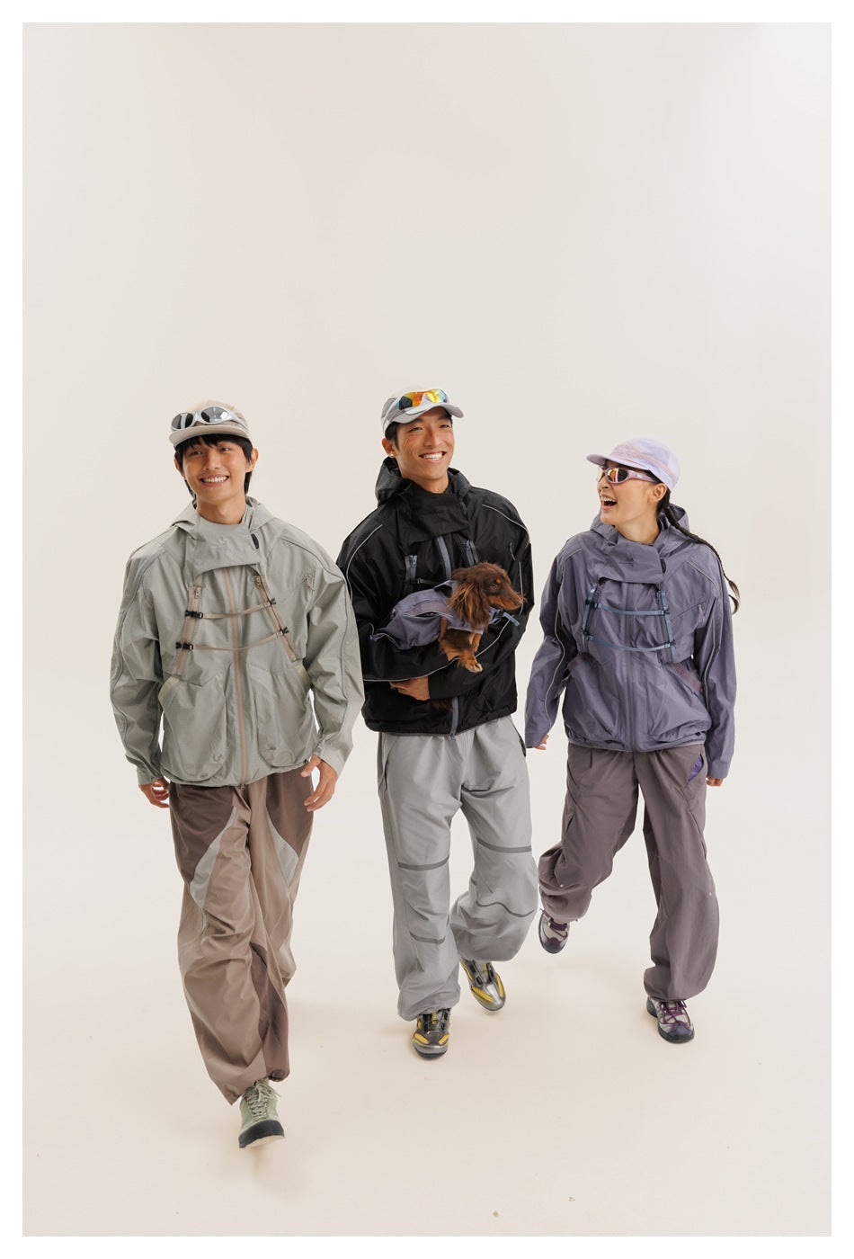 Three models wear hooded outdoor jackets in light gray, black, and lavender, with loose technical-style pants.