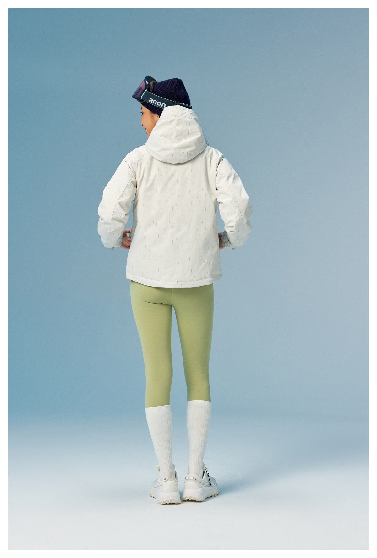 Rear view of a model wearing a white patterned hooded jacket with pale green leggings.