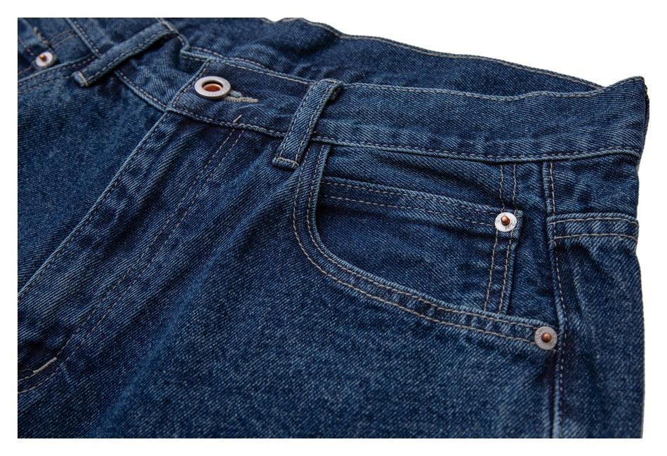 Angled close-up of dark blue jeans showing the waistband and front pocket with metal rivets.