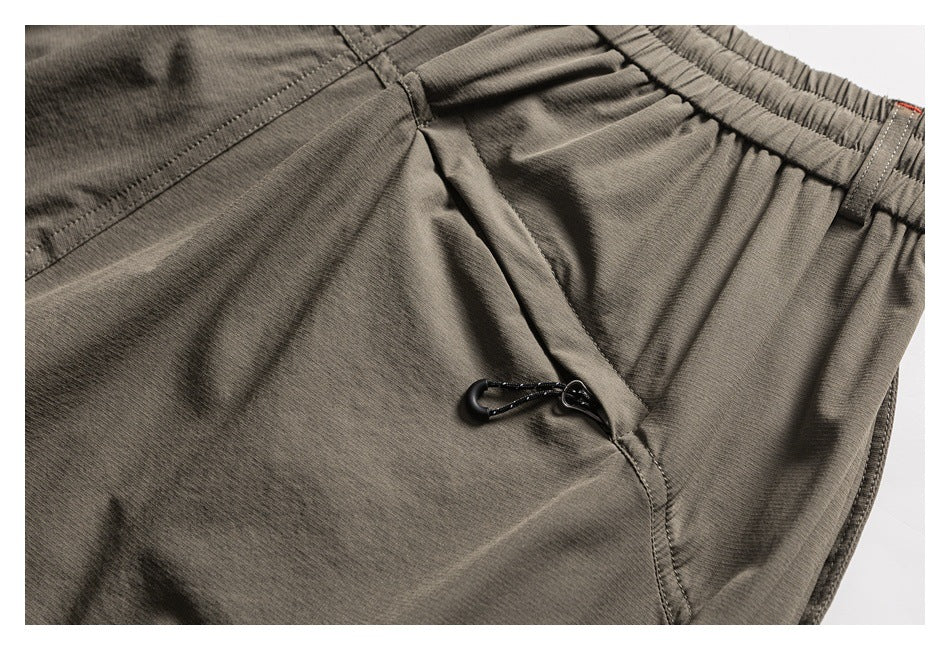 Close-up of taupe trousers with a small black clip attached beside a pocket seam.