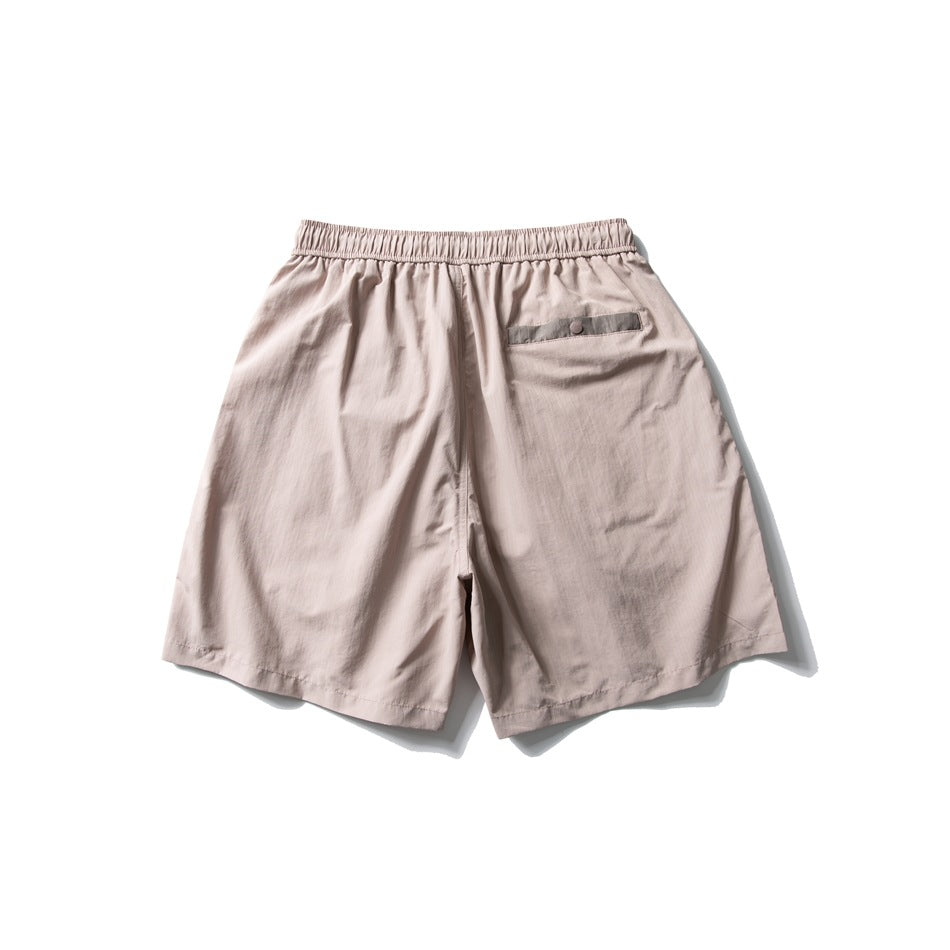 Back view of pale beige shorts with an elastic waistband and a single buttoned rear pocket.