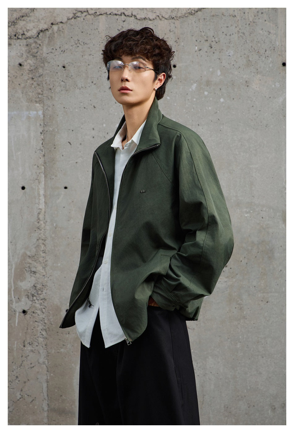Three-quarter view of a person wearing an olive-green zip jacket with a raised collar.