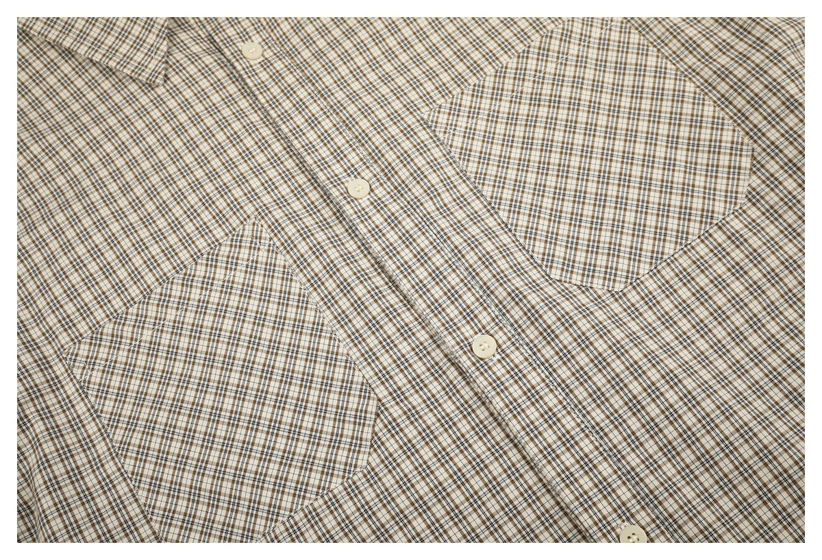Close-up of a beige, brown, and black checked shirt with cream buttons and two patch pockets.
