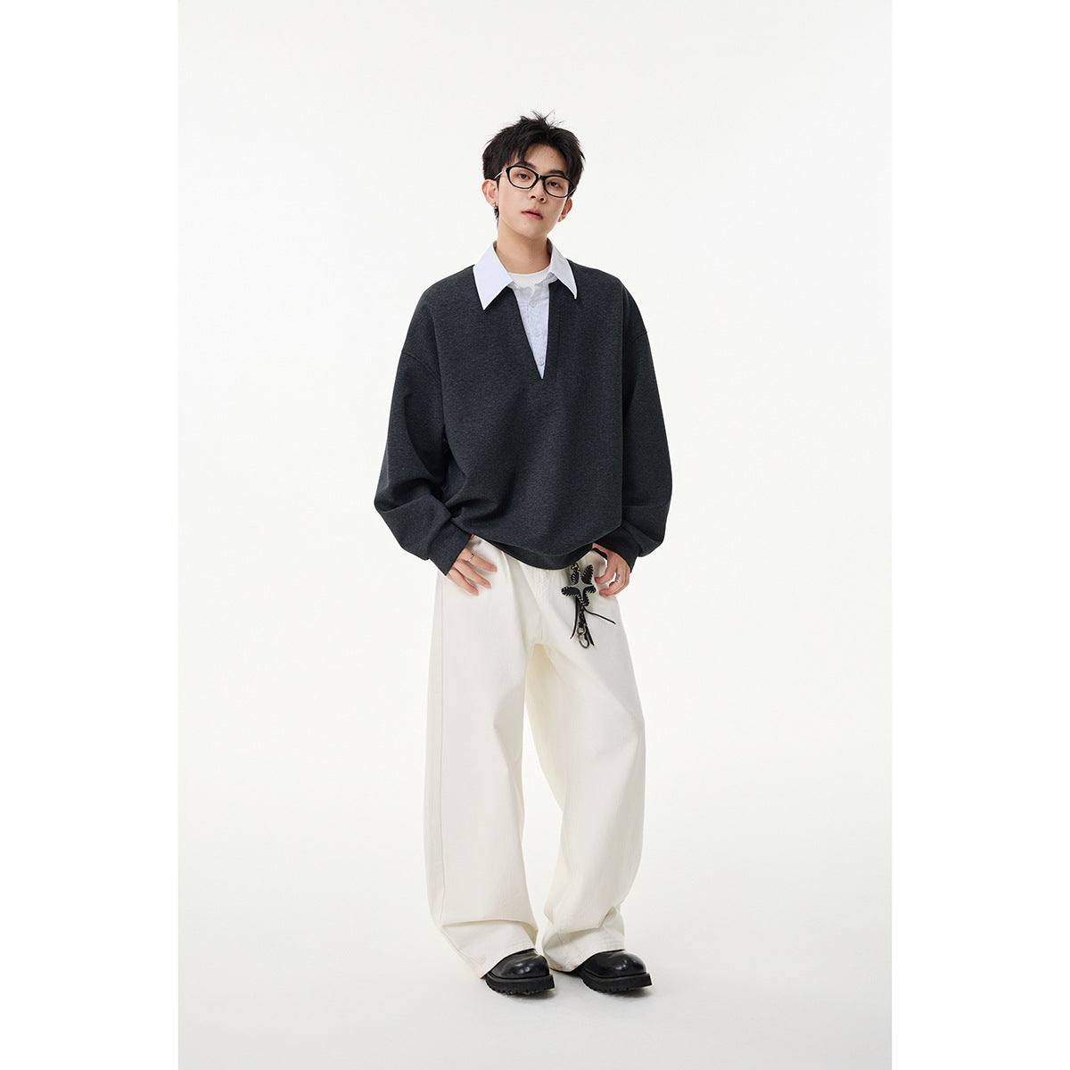 Full-length model wearing a charcoal oversized V-neck sweatshirt with a white collar and loose white trousers.