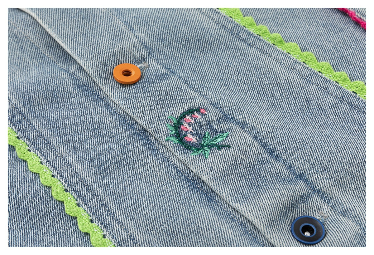 Close-up of a blue denim jacket with lime scalloped trim, orange and blue buttons, and small floral embroidery.