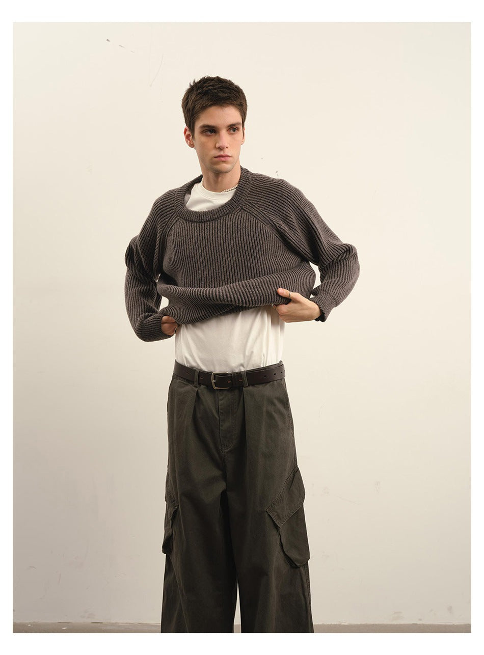 Model lifting a dark taupe ribbed crewneck sweater to show its fit over a white T-shirt.