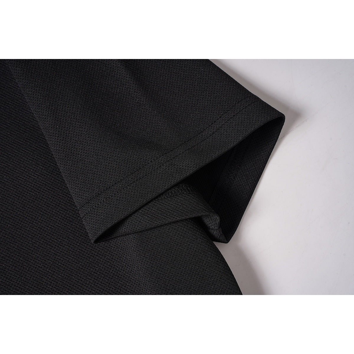 Close-up of the black textured polo's short sleeve and stitched hem.