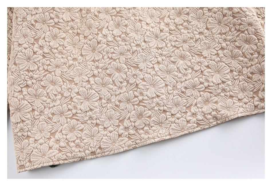 Close-up of the hem of beige floral-embroidered fabric laid flat.