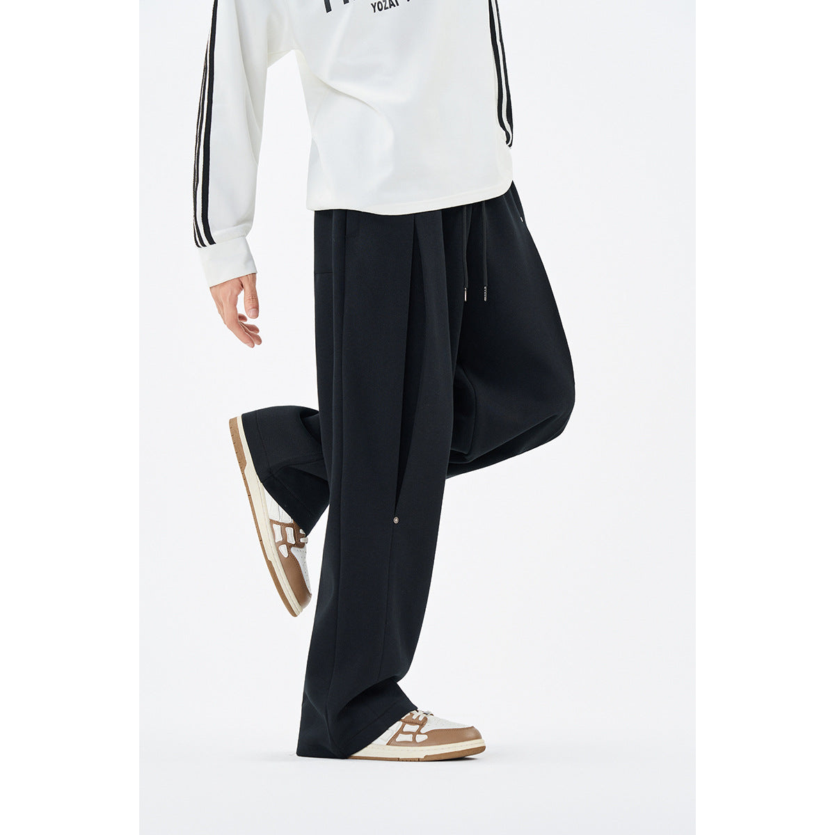 Side view of a model wearing loose black drawstring pants with small metal details and a white striped-sleeve top.
