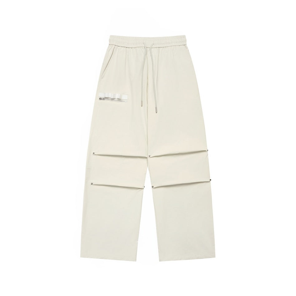 Off-white wide-leg drawstring pants with knee pleats, rivets and a zippered ribbon pocket, flat lay front view