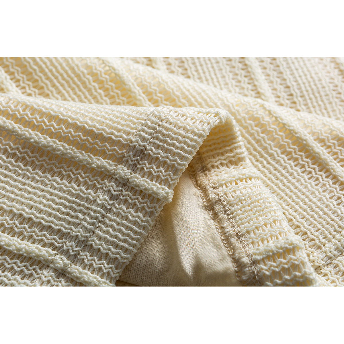Close-up of ivory open-knit fabric with repeating zigzag rows and a stitched seam.