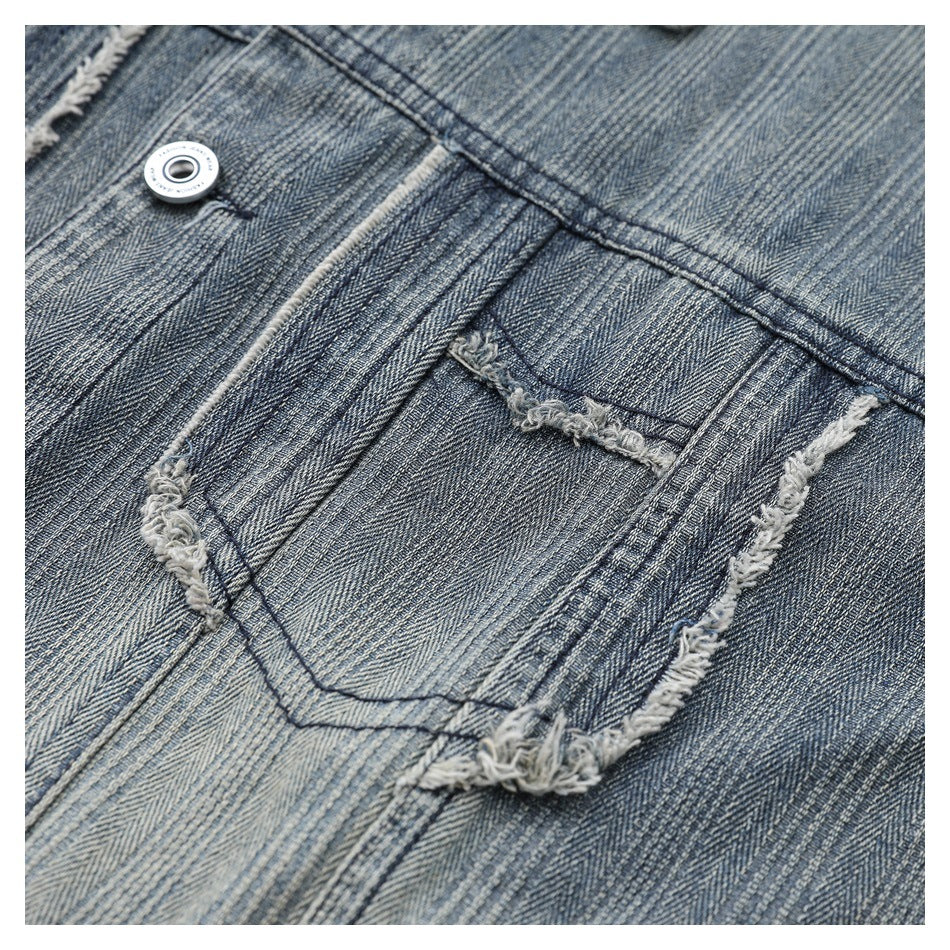 Close-up of a denim chest pocket with frayed edges, visible stitching, and a metal button.