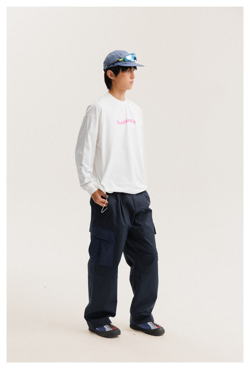 Three-quarter view of a model wearing a white long-sleeve shirt with pink text and navy cargo pants.