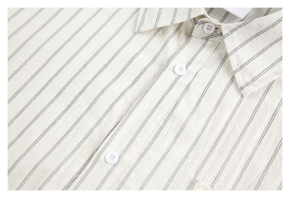 Close-up of an ivory shirt with thin dark stripes, showing the pointed collar and white button placket.