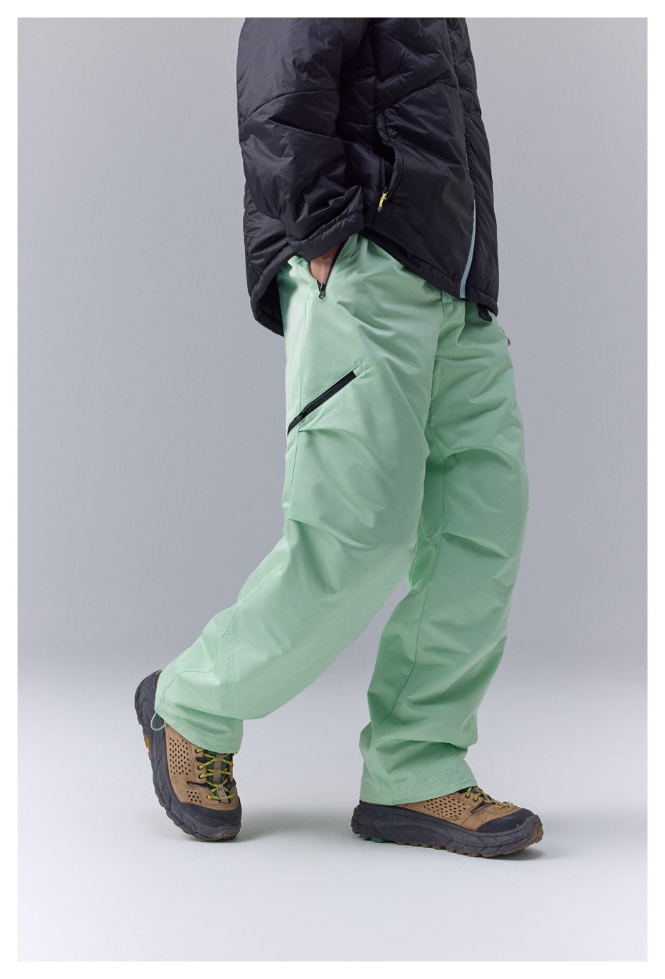 Side view of mint-green loose-fit pants showing a diagonal black zip pocket, worn by a person.
