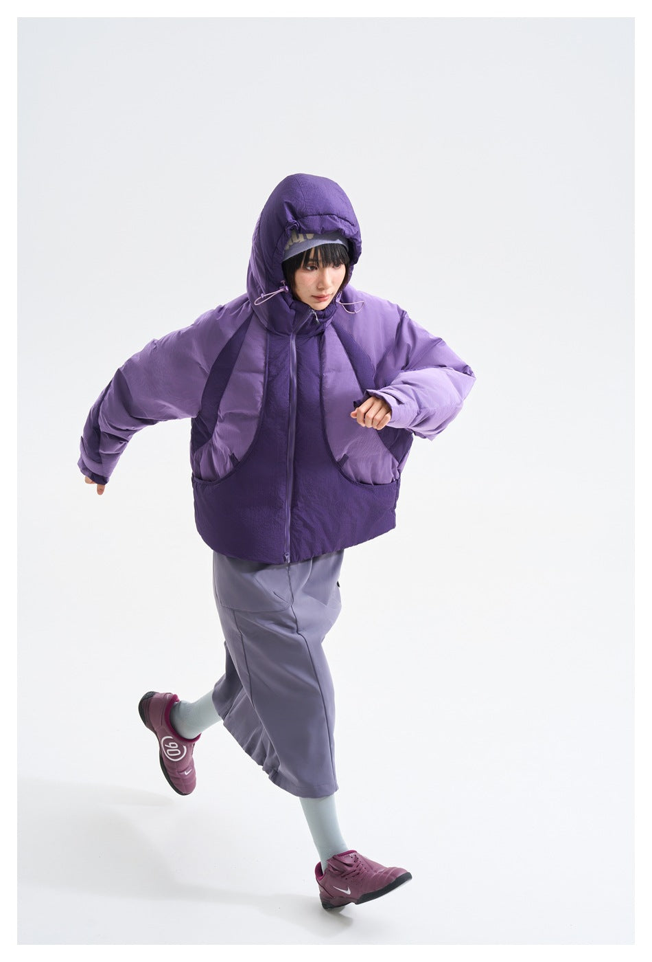 Model running in a purple hooded puffer jacket with a gray-purple skirt and burgundy sneakers