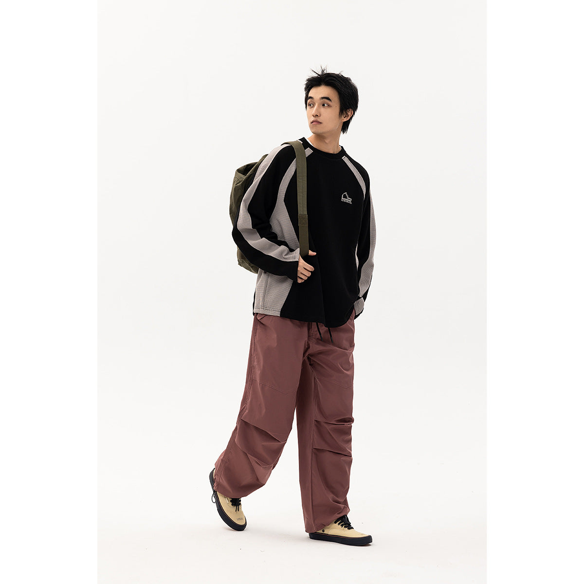 Model wearing a black and gray raglan sweatshirt with dusty mauve pants and an olive backpack.