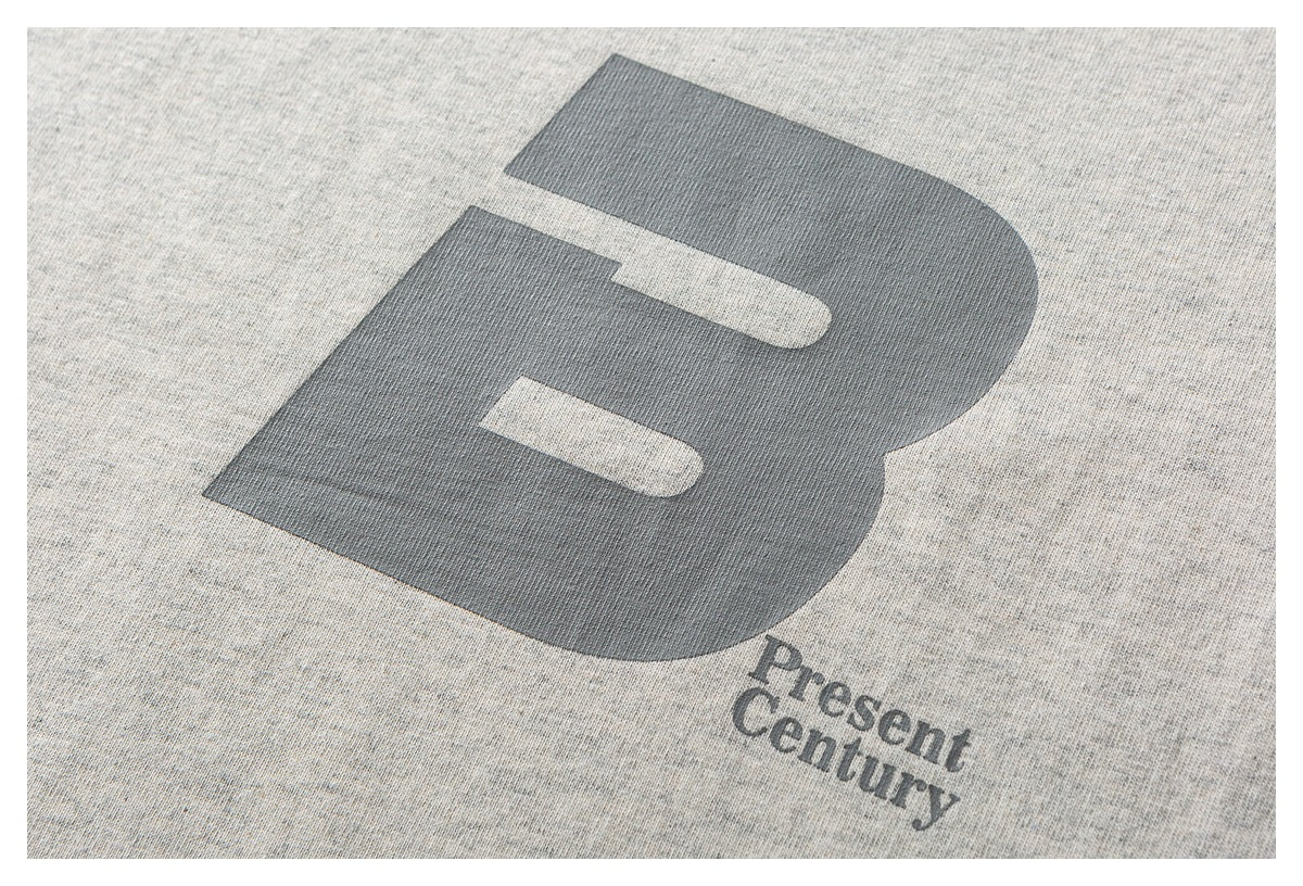 Close-up of a large gray letter graphic and “Present Century” text printed on light gray heathered fabric.