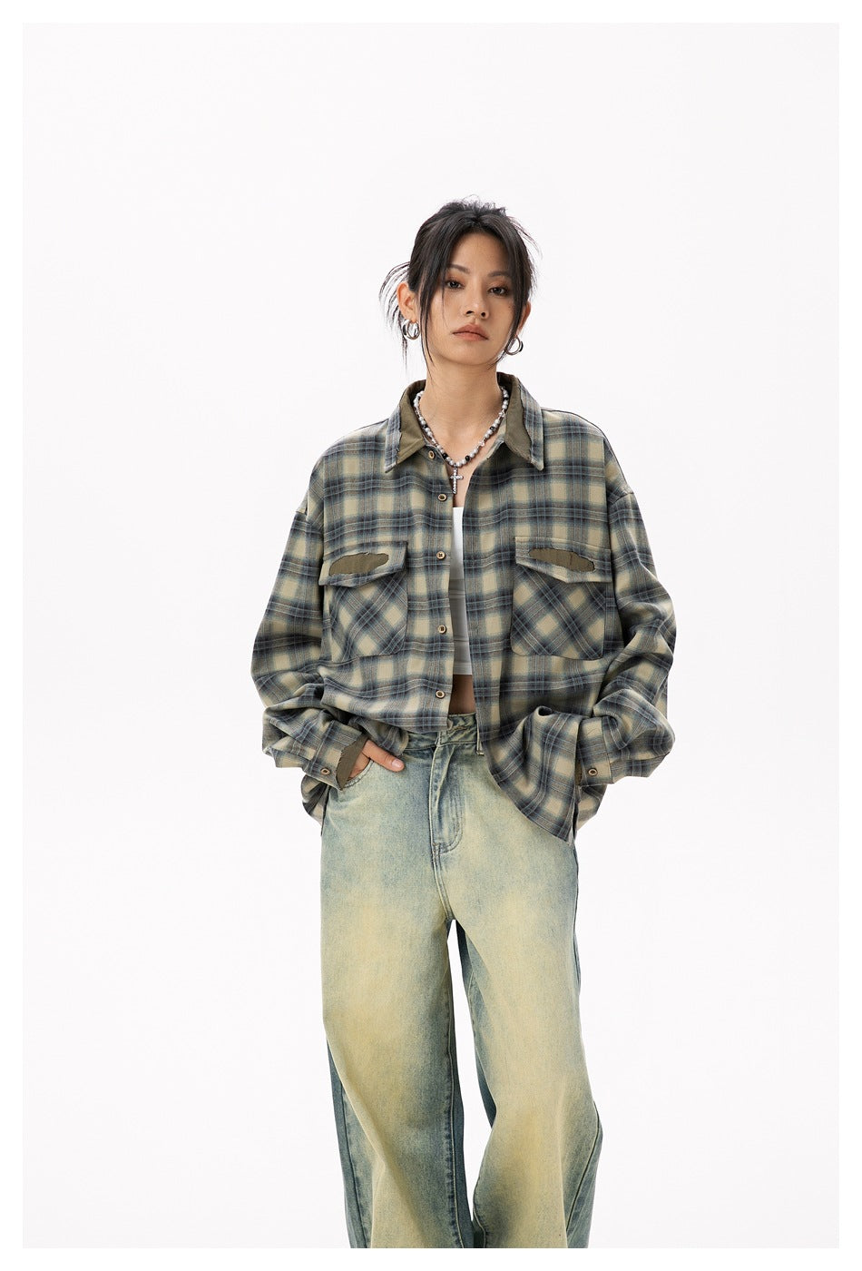 Front view of a model in a cropped olive and blue plaid shirt with distressed chest pockets and loose faded jeans.