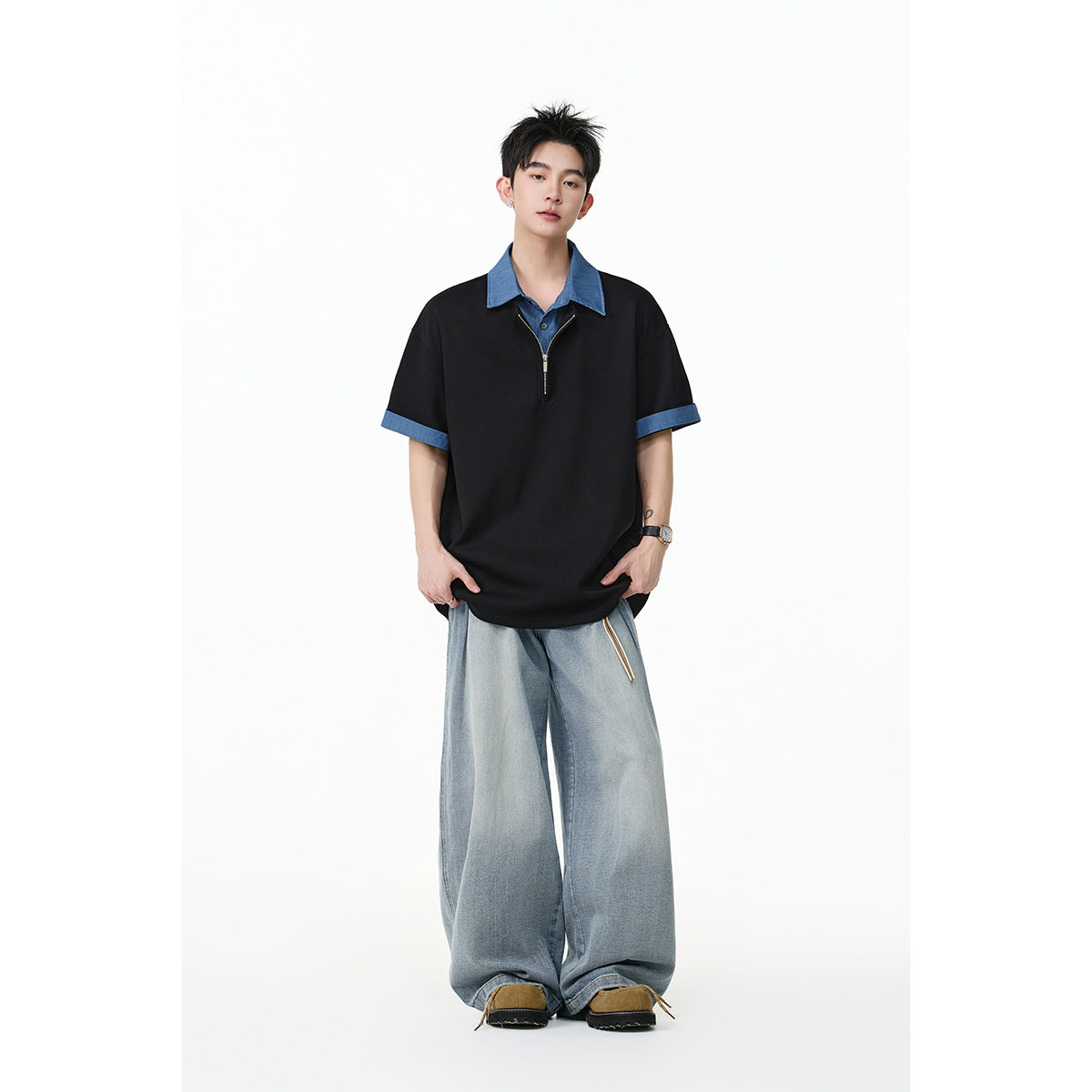 Front view of a model wearing a black short-sleeve quarter-zip polo with blue collar and sleeve cuffs, paired with light-wash