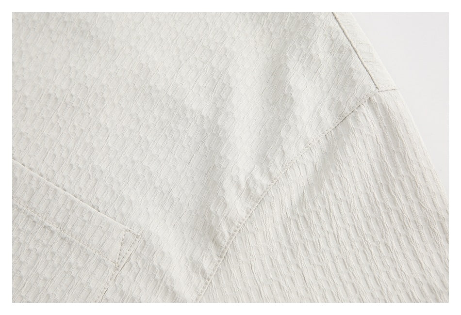 Close-up of ivory textured garment fabric with curved seams and a gathered panel.