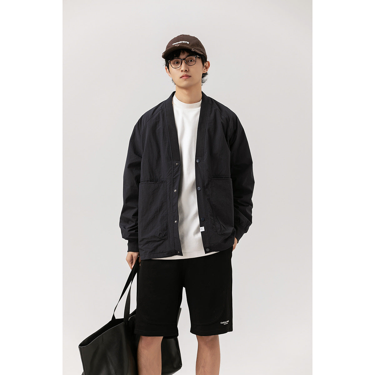 Model wearing a black snap-front cardigan jacket over a white shirt with black shorts.