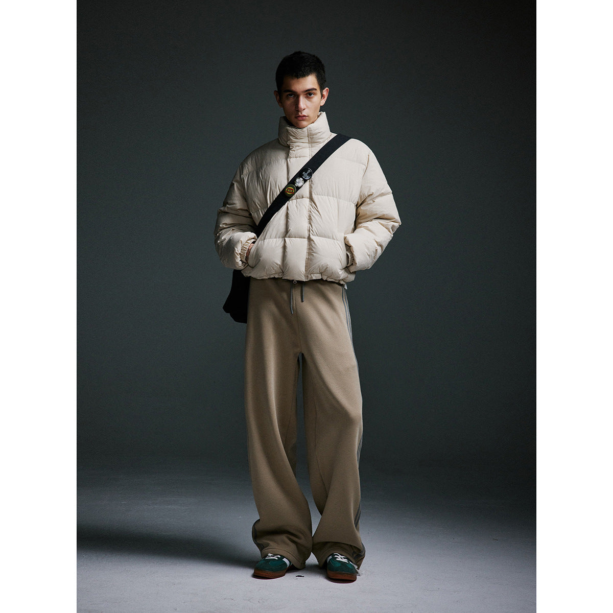 Model wearing an ivory puffer jacket with a black crossbody bag and loose taupe trousers.