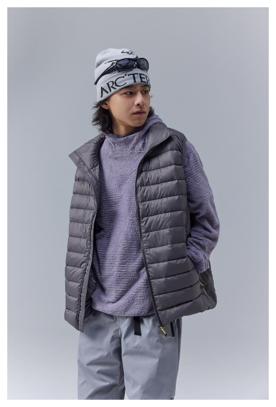 Person wearing an open dark gray quilted puffer vest over a purple textured fleece-like top and gray pants