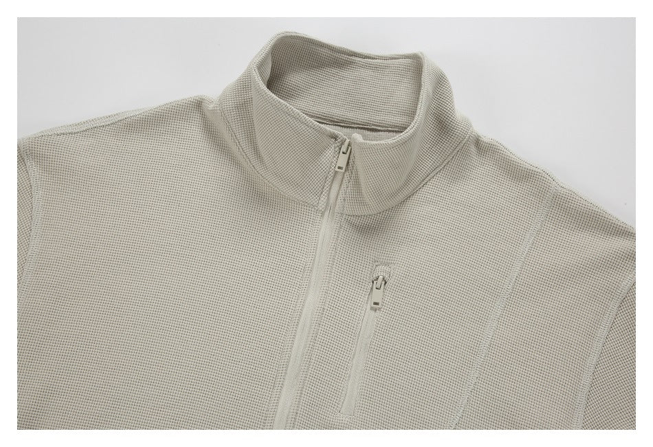 Close-up of a light beige textured pullover with a stand collar, front zipper, and vertical chest zip pocket.