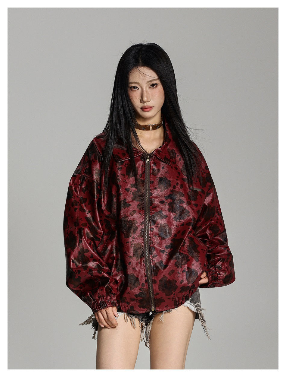 Model wearing a glossy burgundy jacket with a black irregular print, front zip, wide sleeves and elastic cuffs.