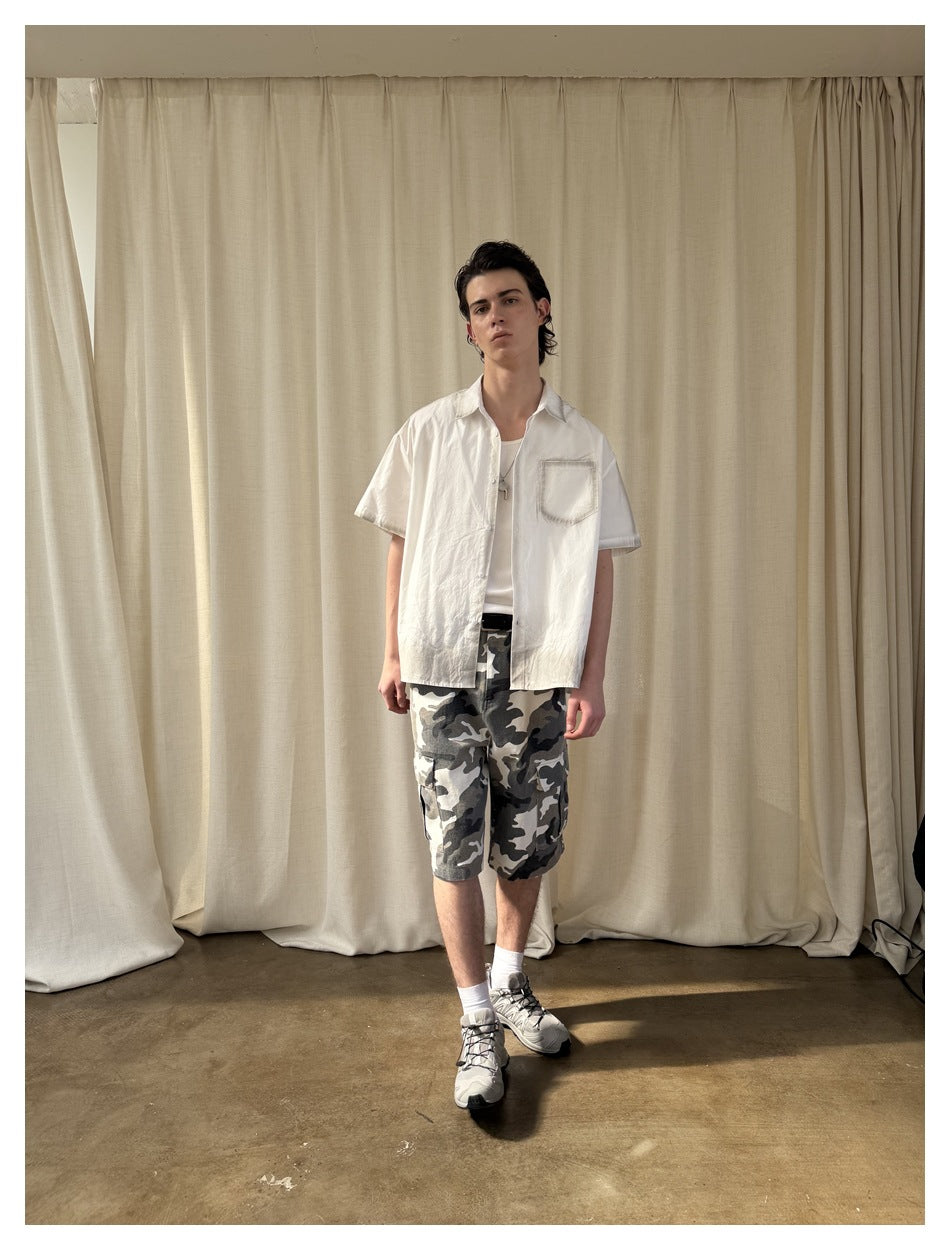 Full-length front view of a model wearing a white short-sleeve shirt and gray camouflage cargo shorts.