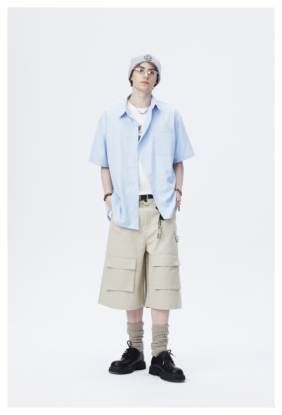 Model wearing a light blue short-sleeve button-up shirt with a chest pocket and beige cargo shorts.