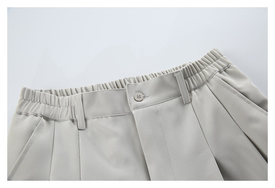 Close-up of light gray trousers showing the elasticated waistband, button closure, belt loops and front pleats.