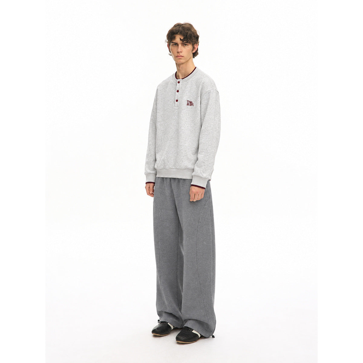 Three-quarter front view of a model in a light gray button-neck sweatshirt and wide-leg dark gray pants.