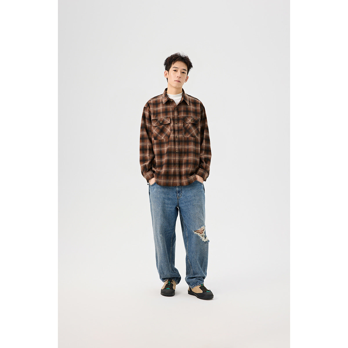 Front view of a model in a brown plaid overshirt with two flap chest pockets, layered over a white top with blue jeans.