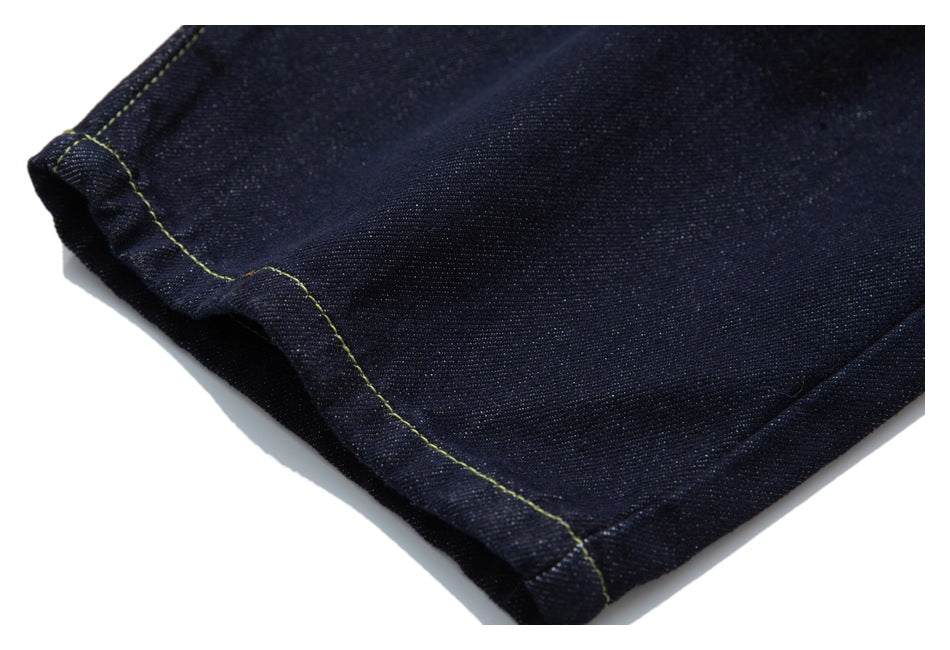 Close-up of a cuffed hem on dark indigo jeans with contrast stitching.