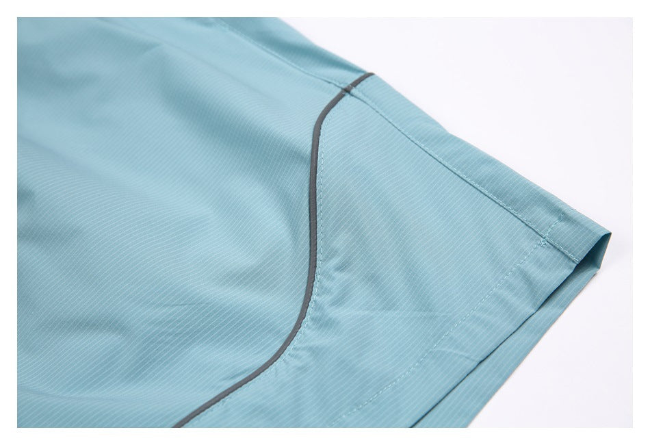 Close-up of aqua shorts showing a curved gray-piped seam and stitched hem.