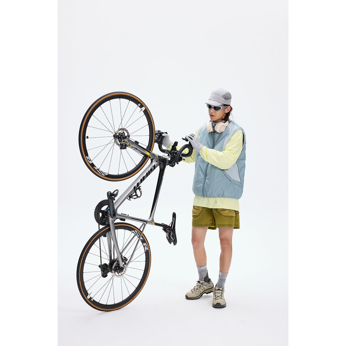 Model wearing a pale blue sleeveless vest over a yellow long-sleeve top beside an upside-down bicycle.