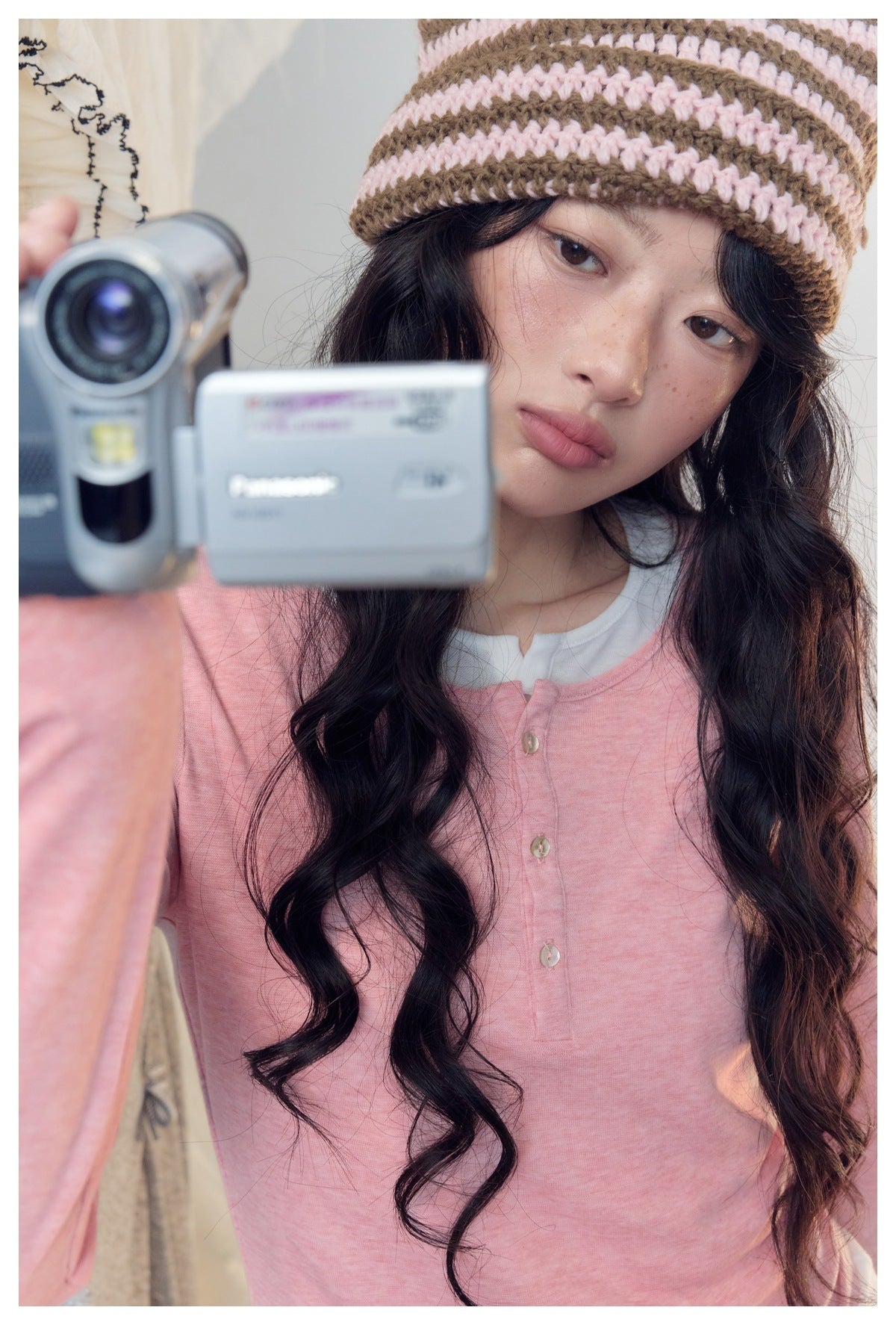 Close-up of a model wearing a pink button-front henley and a brown-and-pink striped knit hat.