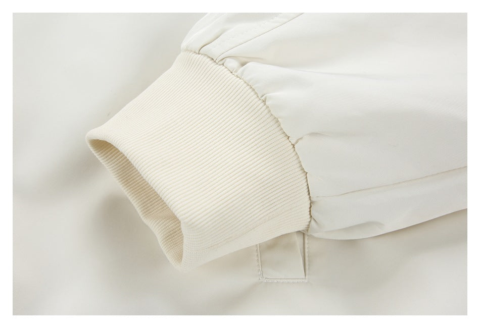 Close-up of a cream ribbed sleeve cuff and a small pocket flap on a white garment.